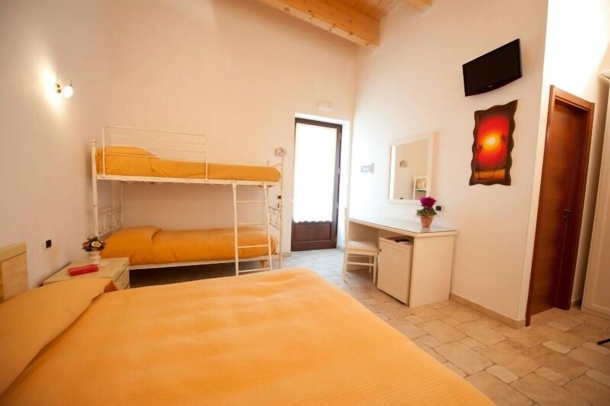 Une chambre avec des lits superposés, un bureau, une chaise, un téléviseur et une porte.