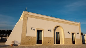A building with a flat roof, a central arched doorway, and four wall-mounted light fixtures.