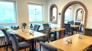 Un restaurant doté de nombreuses tables et chaises, d’arches en briques et de grandes fenêtres.
