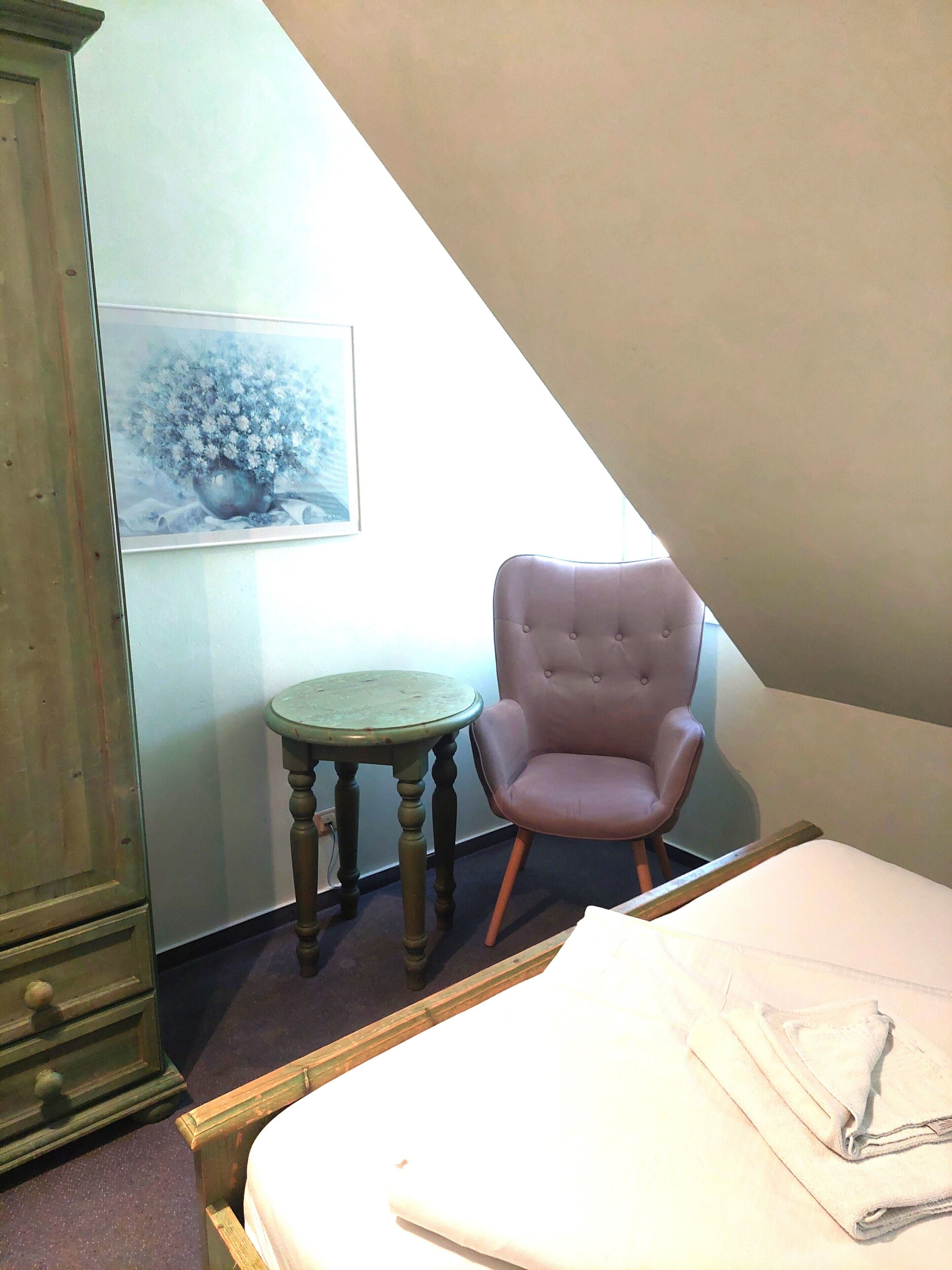 A bedroom with a bed, a chair, a small table, and a cabinet.