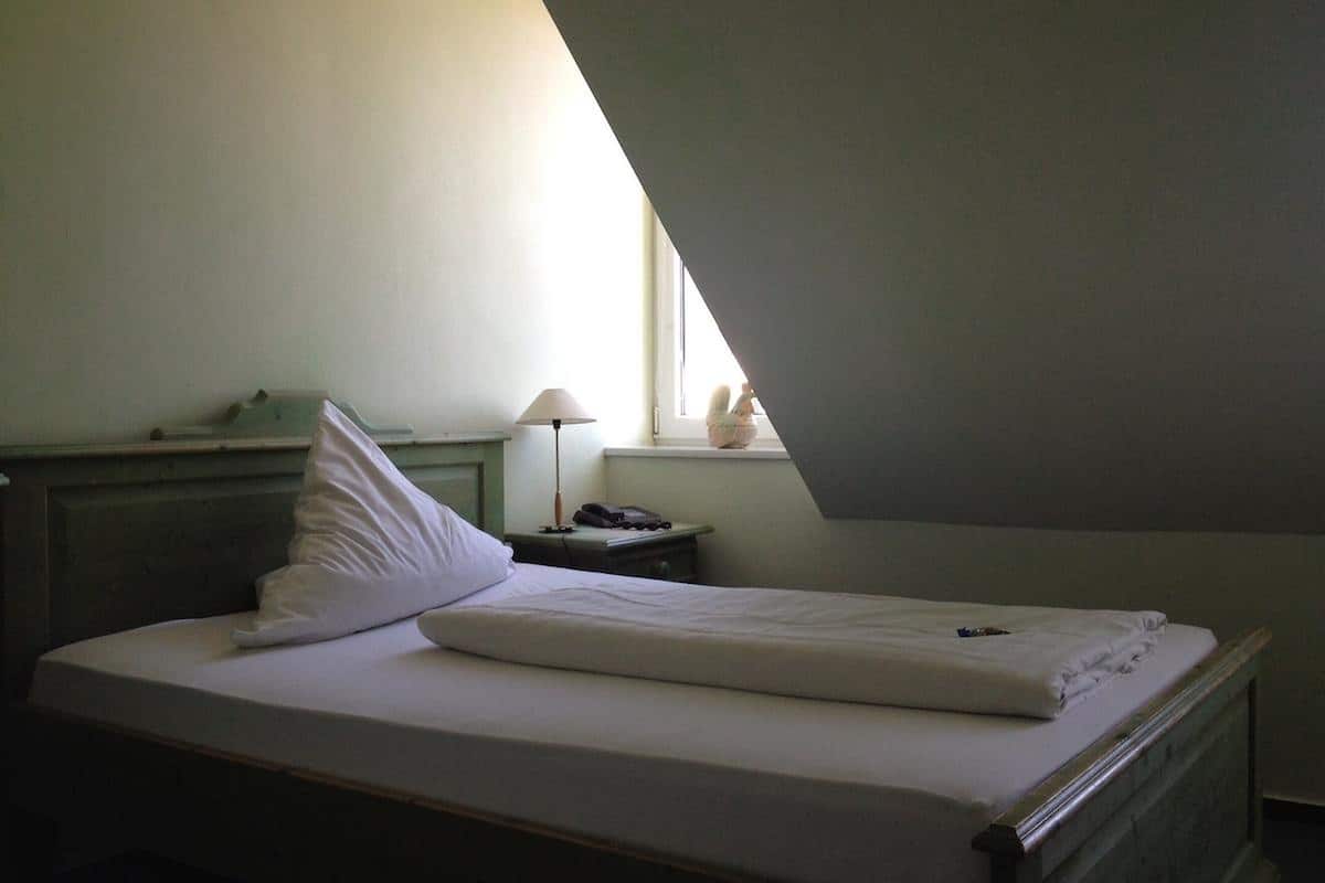 Ein Schlafzimmer mit einem Einzelbett, einem Nachttisch, einer Lampe und einem Fenster mit Blick nach draußen.