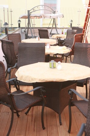 An outdoor patio with wicker furniture and tables, featuring a view of the building in the background. - Hotel Villa Weststrand (Borkum)