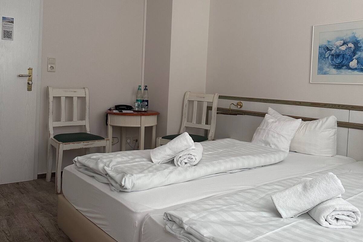 Ein Hotelzimmer mit einem großen Bett, zwei Sesseln, einem kleinen Tisch mit Toilettenartikeln und einem Gemälde an der Wand.