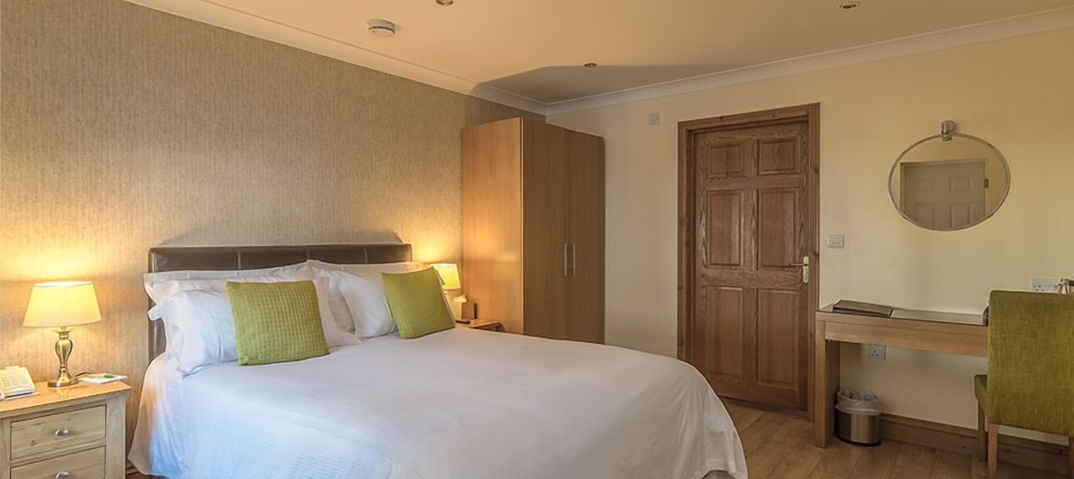 Hotelkamer met een bed, bedlampen, een houten kledingkast, een bureau met stoel en een spiegel.