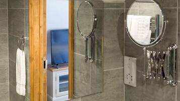A bathroom with a large mirror, a towel rack, and a shower with a handheld showerhead.