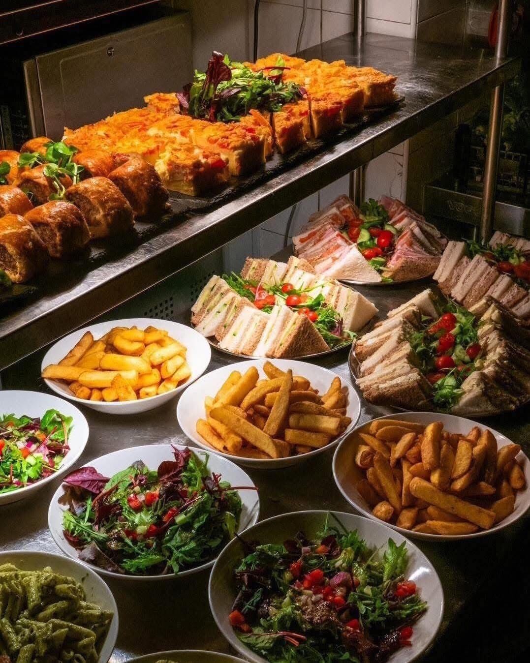 Buffet-pöydässä on tarjolla monenlaisia ruokia, kuten voileipiä, ranskalaisia perunoita ja salaatteja.