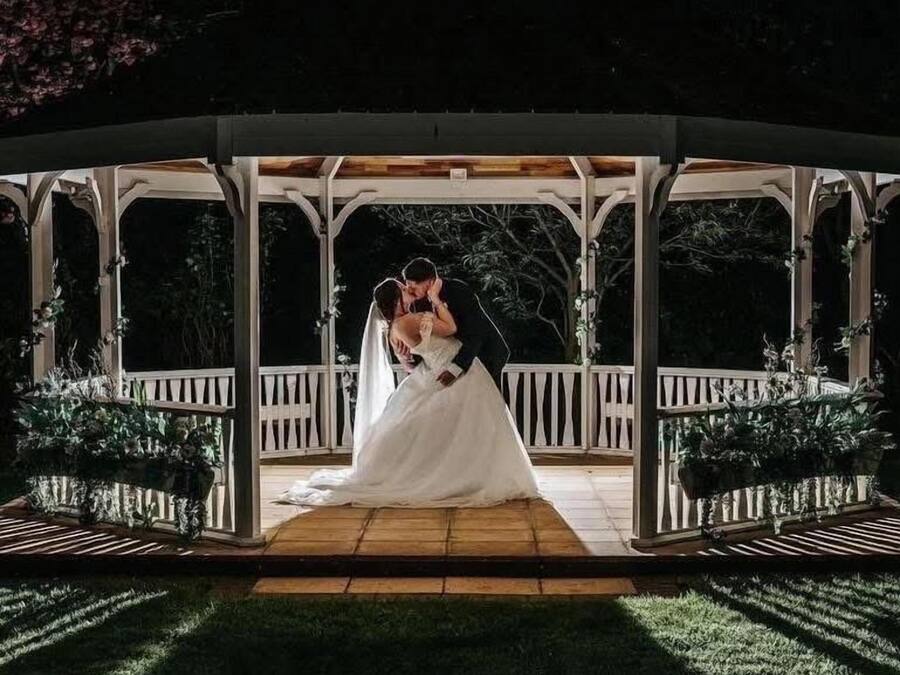 A gazebo with a wooden floor and white railings, surrounded by greenery.