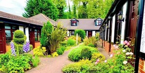 A courtyard with a brick pathway, surrounded by well-maintained hedges and flowering plants. - The Stanwick Hotel (Wellingborough)