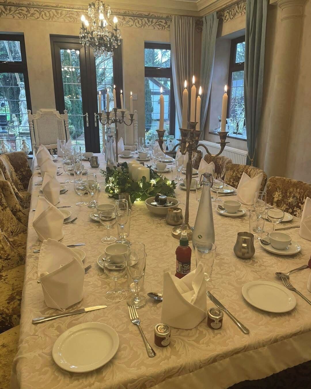 Un comedor formal con una larga mesa dispuesta para una comida, rodeado de sillas ornamentadas y un candelabro.