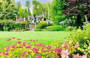Una casa tradicional rodeada de abundante vegetación y un jardín bien cuidado con diversas flores.
