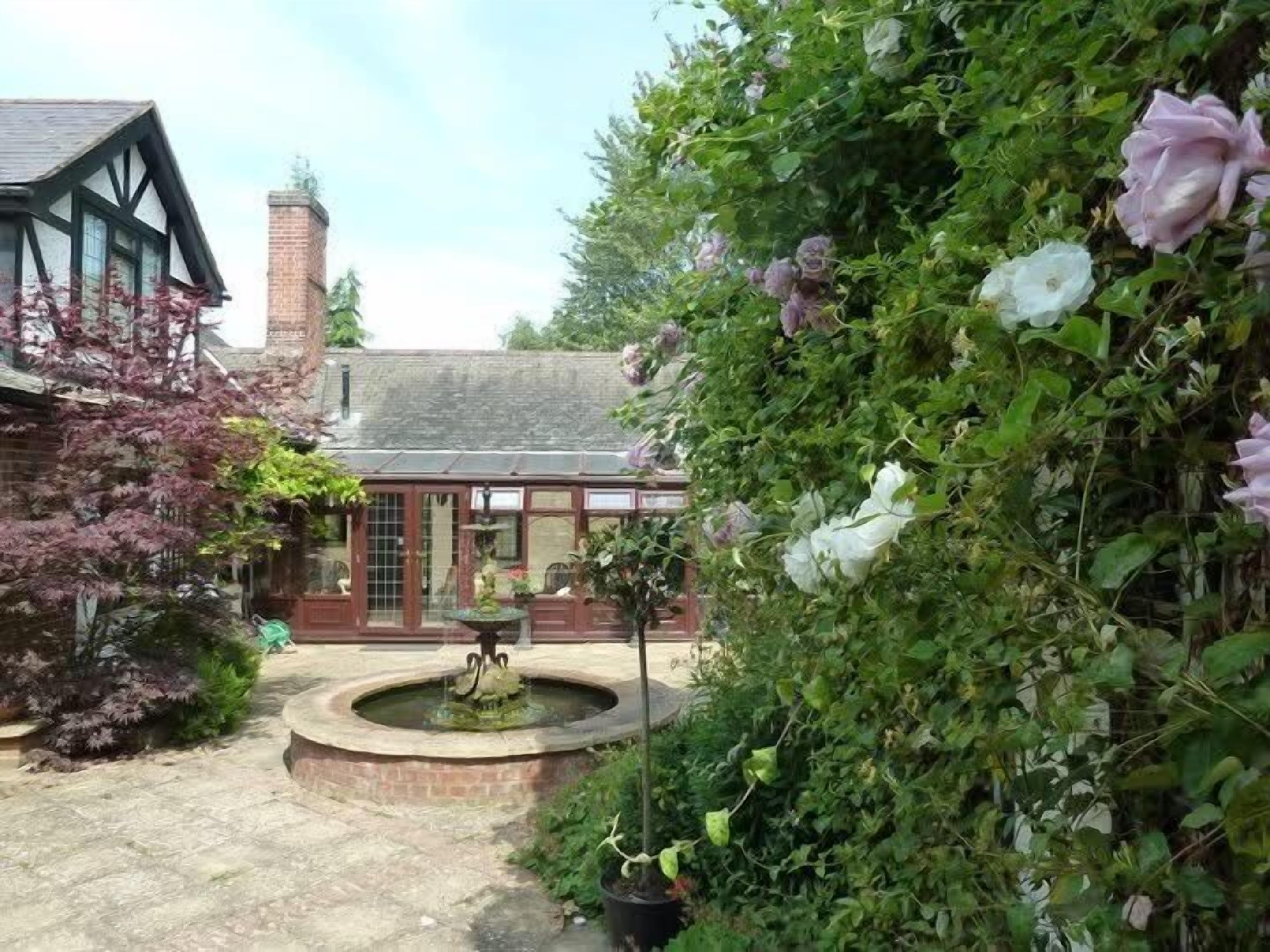 A traditional building with a brick chimney, a circular fountain, and a garden with flowering plants.