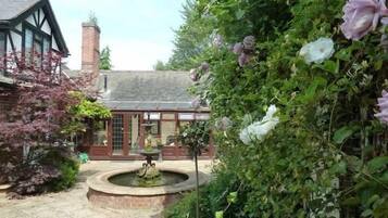 A traditional building with a brick chimney, a circular fountain, and a garden with flowering plants.