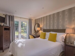 A hotel room with a large bed, a desk with a lamp, a chair, and a wardrobe. - The Stanwick Hotel (Wellingborough)