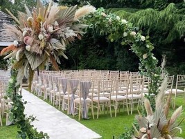 Un salón de bodas al aire libre con filas de sillas blancas y un arco floral.
