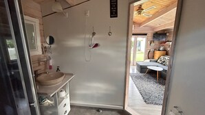 A bathroom with a sink, mirror, and towel rack. A door leads to a living area with a sofa and a TV. - Piccobello Bed & Breakfast (Koge)