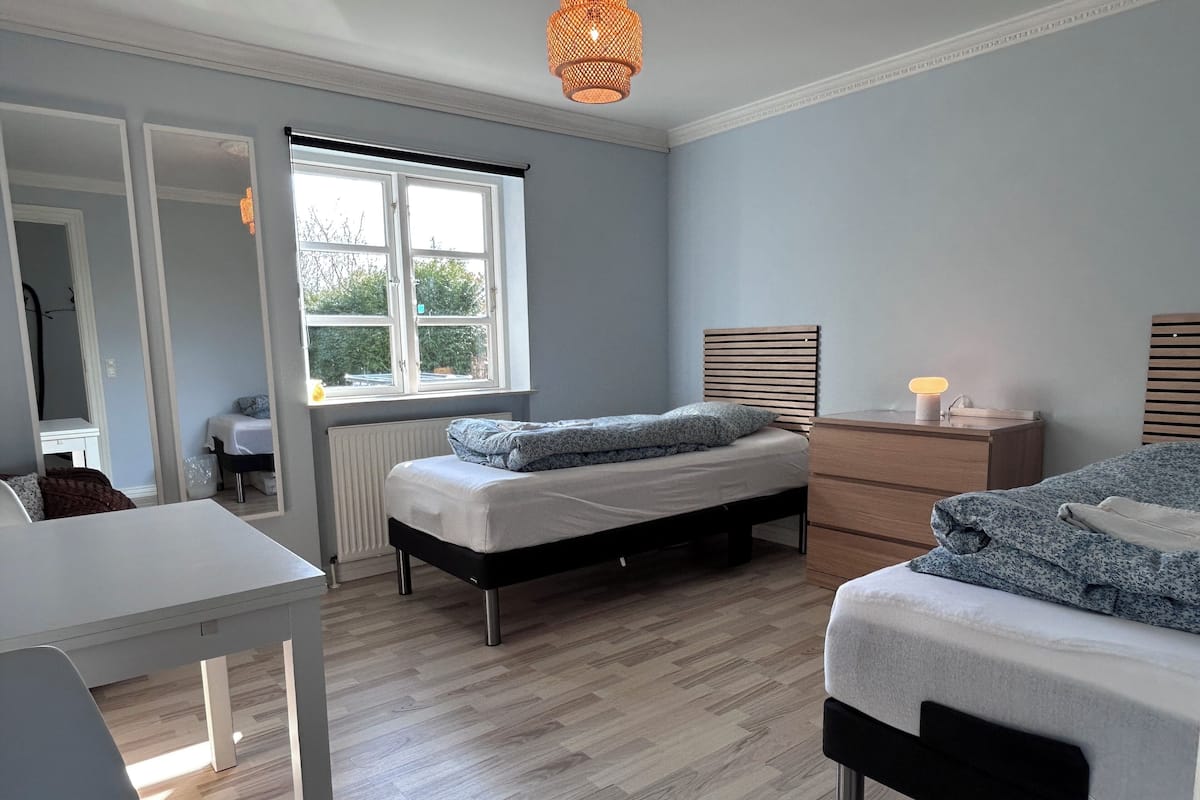 A bedroom with a bed, bedside table, dresser, and a window with a view of greenery.