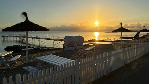 A beach scene with a wooden pier, beach chairs, and thatched umbrellas. - Piccobello Bed & Breakfast (Koge)