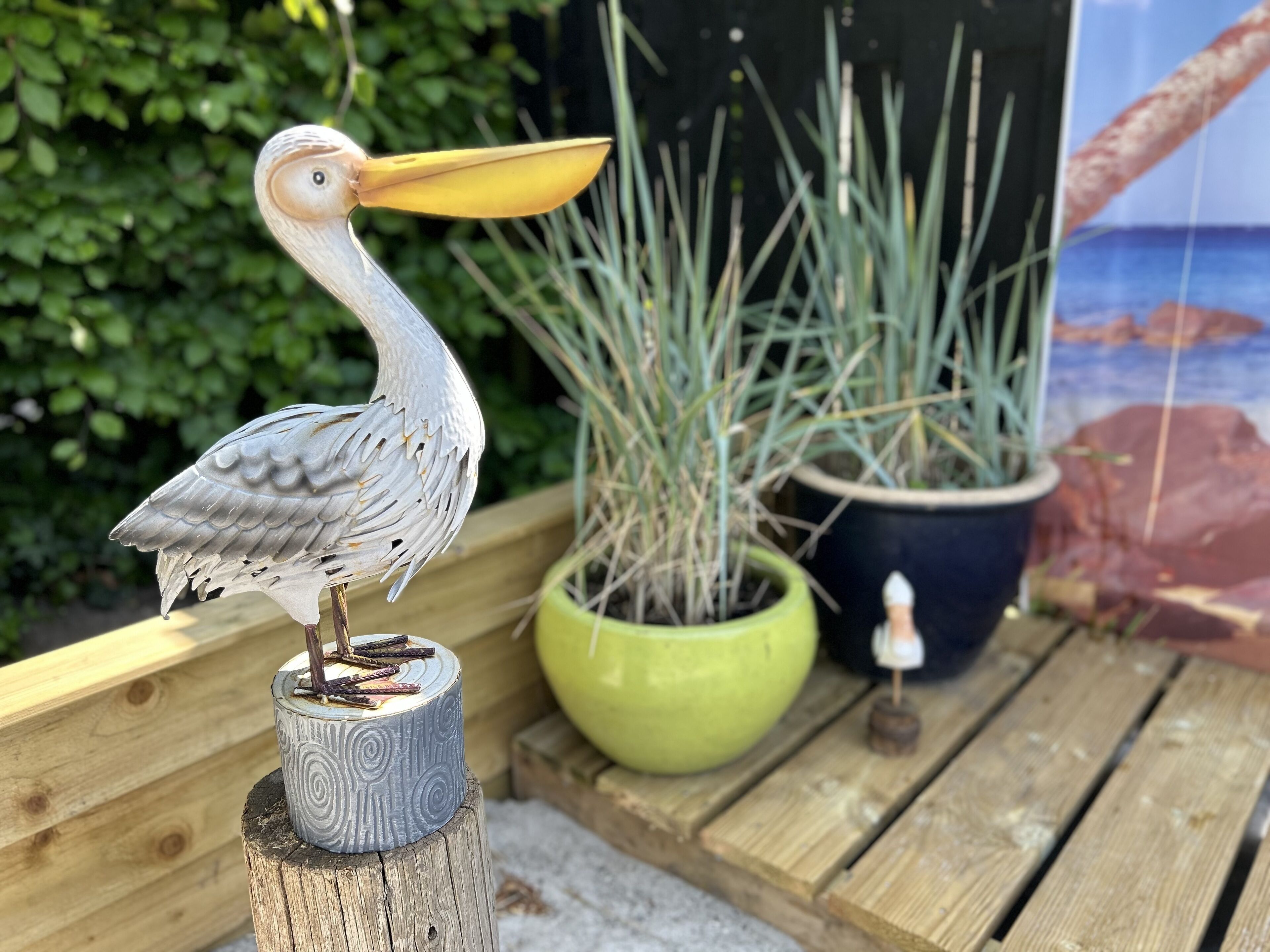 A wooden post with a bird sculpture, a green potted plant, and a blue pot with a small figurine.