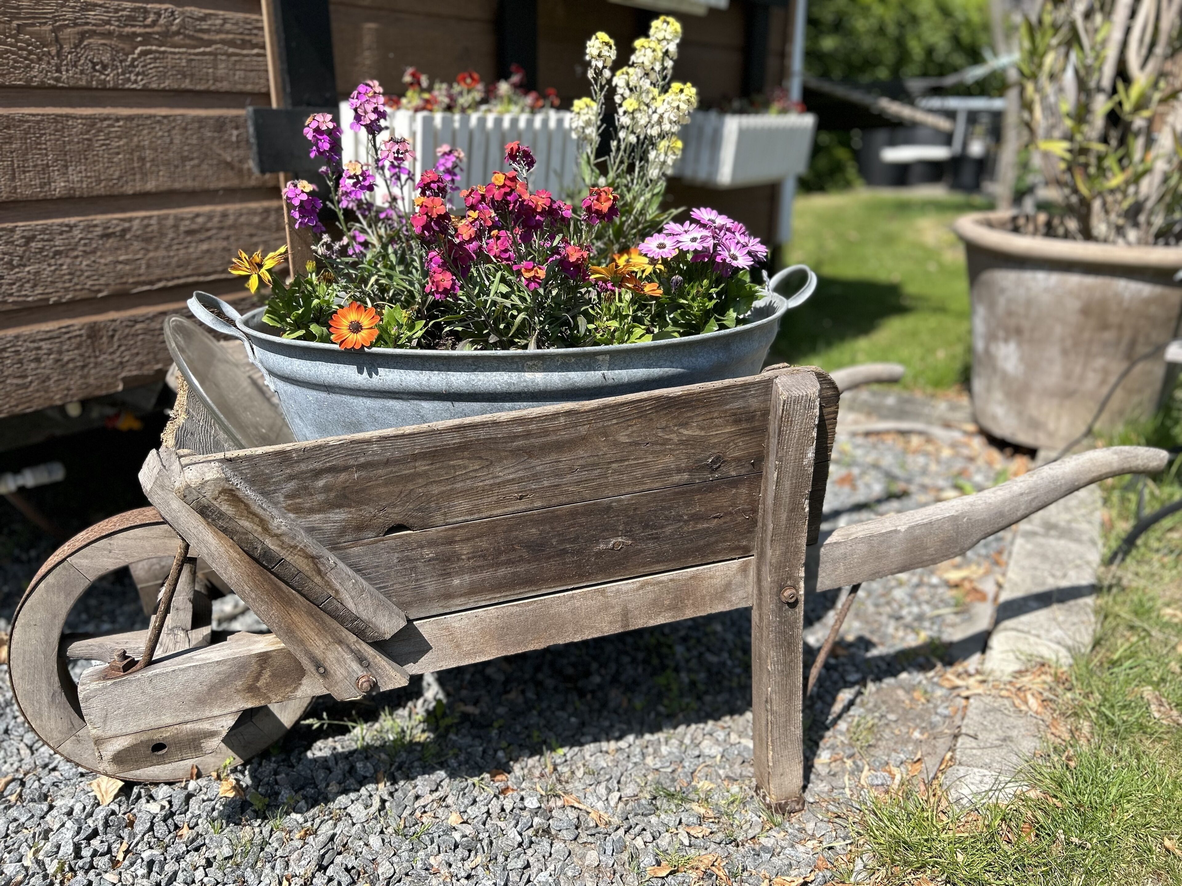 A wooden wheelbarrow with a metal flower pot filled with colorful flowers.