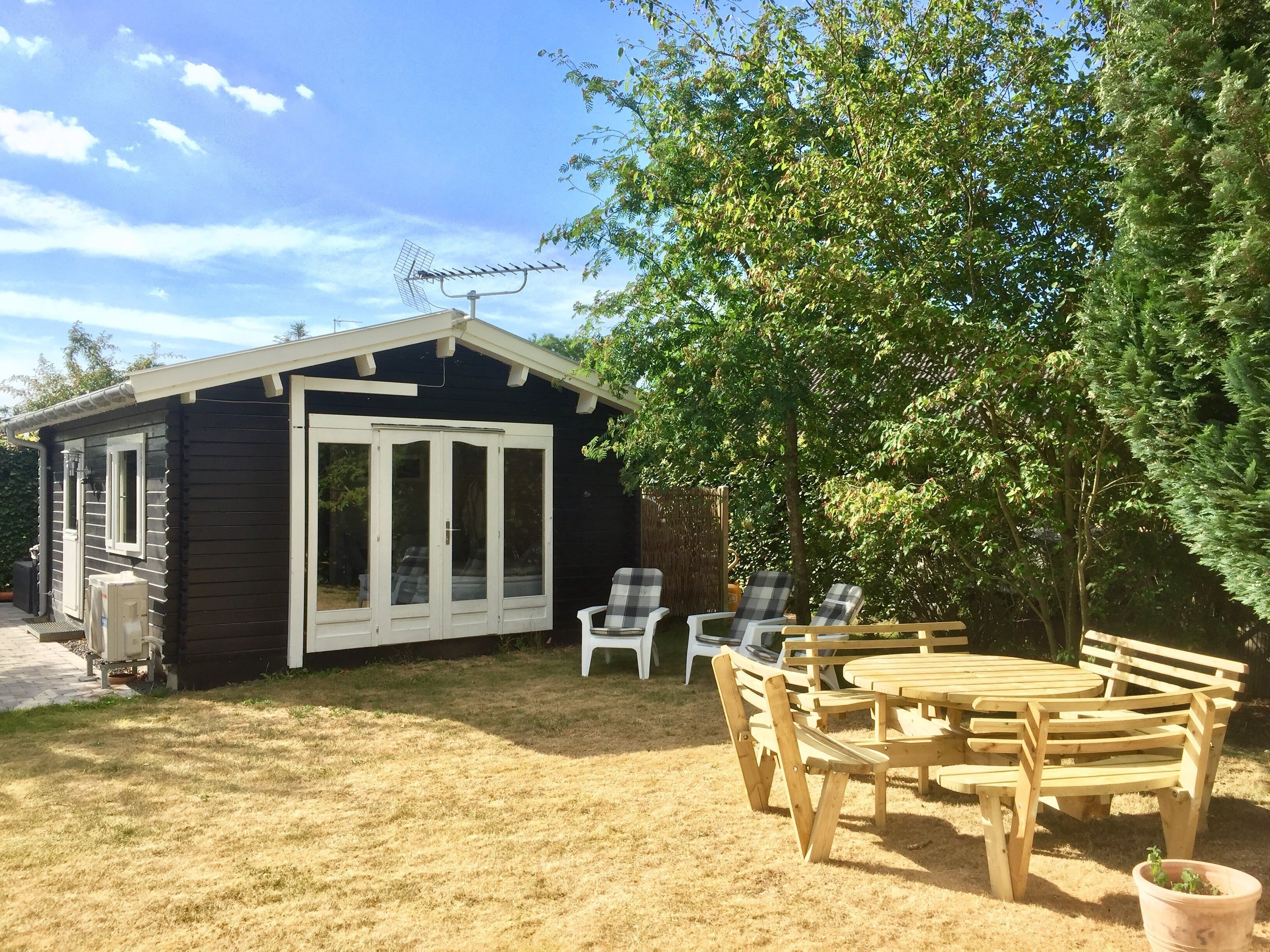 A small cabin with a sliding glass door, a patio with wooden furniture, and a tree providing shade.