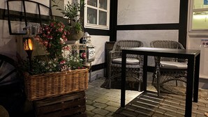 A cozy outdoor seating area with wicker furniture and a table, surrounded by potted plants and a decorative lamp. - Piccobello Bed & Breakfast (Koge)