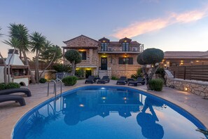 Vista de una piscina junto a una casa de piedra con mobiliario exterior y un muro de piedra.