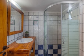 Un baño con tocador de madera, lavamanos blanco, cabina de ducha de vidrio y paredes con azulejos.