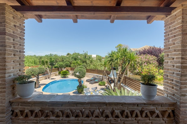 Vista de una piscina rodeada de vegetación, con un muro de piedra y una pérgola de madera.