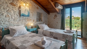 Un dormitorio rústico con paredes de piedra, vigas de madera, dos camas con sábanas blancas, un cuadro y vistas al exterior.