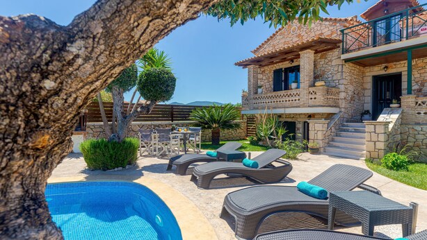 Una villa de piedra con piscina, sillones de descanso y una escalera que lleva a un balcón.