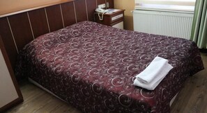A hotel room with a bed, a nightstand, a telephone, and a radiator. - Yeni Hotel (Malatya)