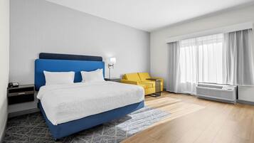 A modern hotel room with a large bed, a bedside table, a lamp, a sofa, and a window with curtains.