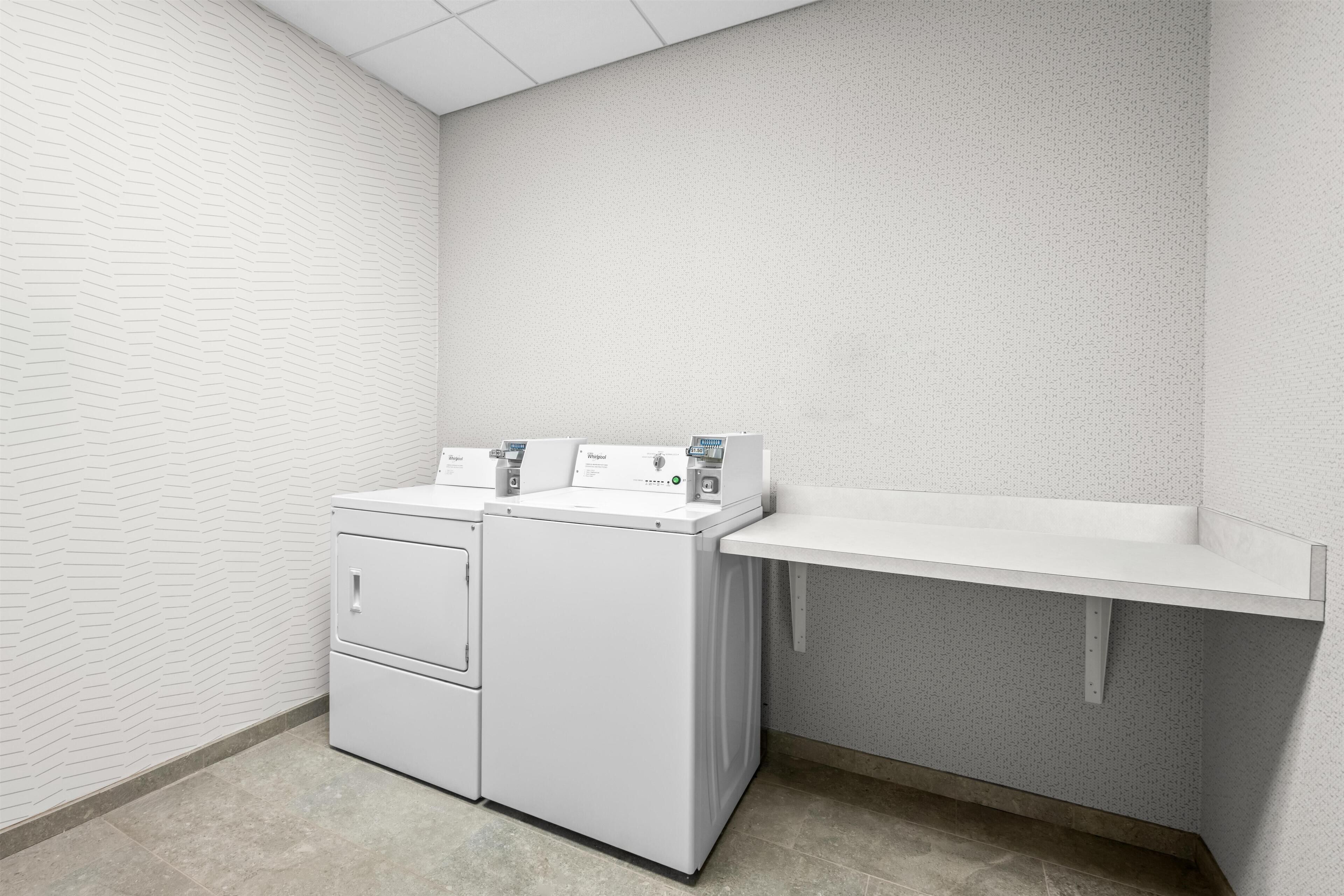 A laundry room with two stacked washers and dryers, a countertop, and a textured wall.