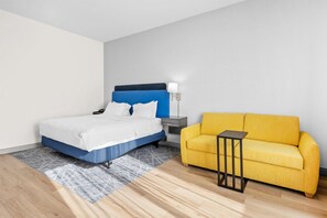 A hotel room with a bed, a nightstand, a lamp, a sofa, and a small table. - Hampton Inn & Suites Knightdale Raleigh (Raleigh)
