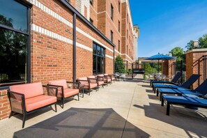 An outdoor patio with brick walls, lounge chairs, and tables. - Hampton Inn & Suites Knightdale Raleigh (Raleigh)