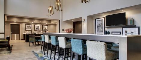 Une cuisine moderne dotée d’un grand îlot central, de tabourets de bar, de luminaires suspendus et d’un téléviseur à écran plat fixé au mur.