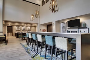 Une cuisine moderne dotée d’un grand îlot central, de tabourets de bar, de luminaires suspendus et d’un téléviseur à écran plat fixé au mur.