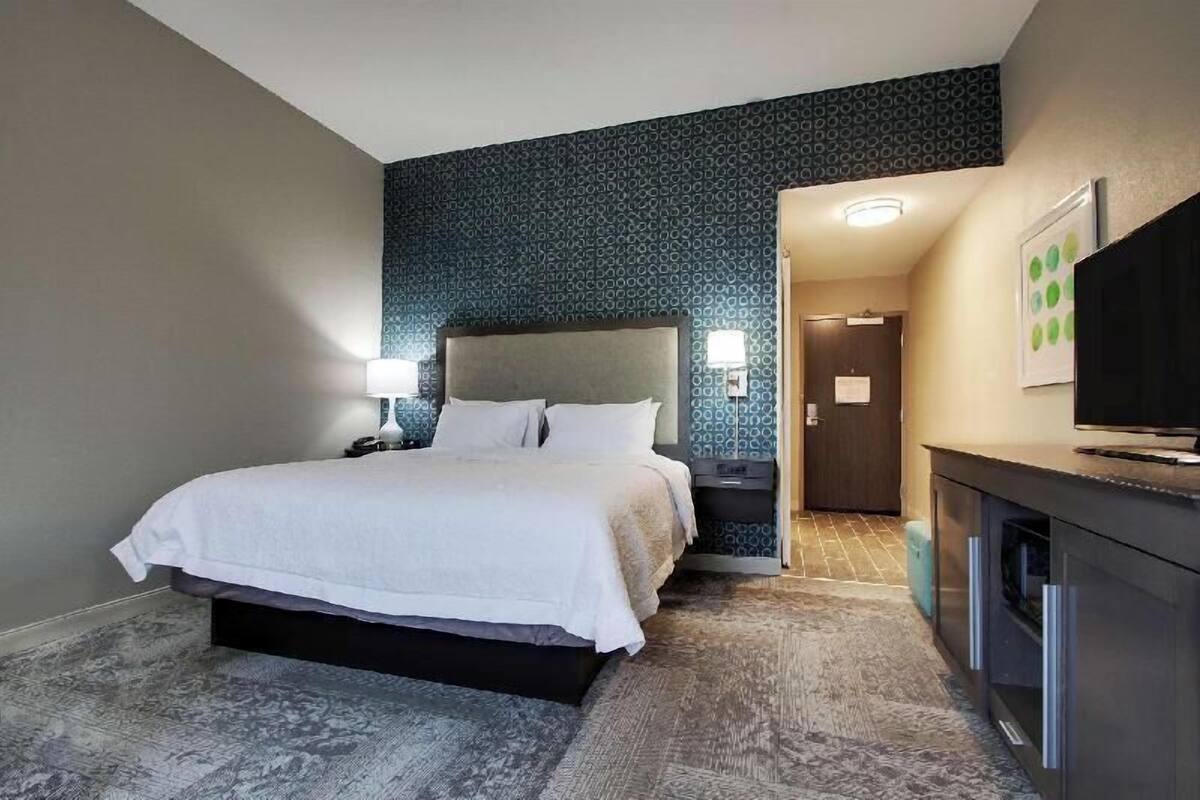 A hotel room with a bed, bedside tables, a TV, and a patterned wall.