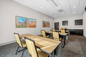 A conference room with tables and chairs, a kitchen area, and artwork on the walls. - Hampton Inn & Suites Knightdale Raleigh (Raleigh)