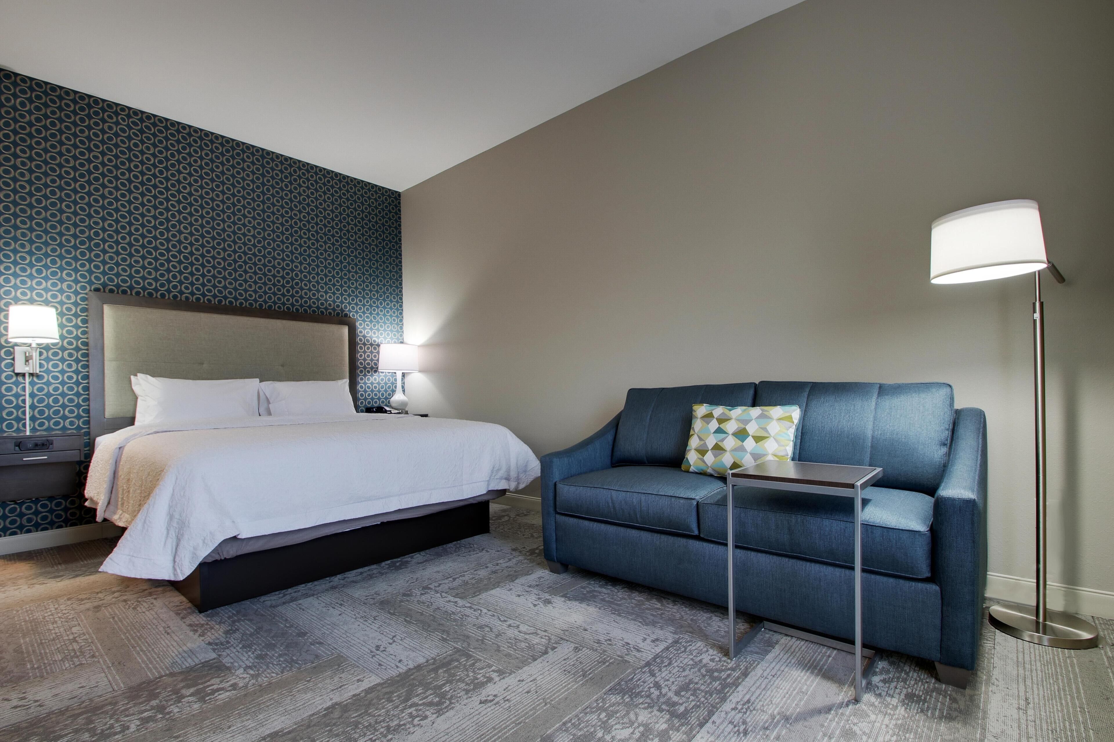 Una habitación de hotel con cama, sofá, lámpara y un papel tapiz estampado.