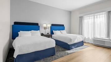 A hotel room with two beds, a nightstand, a lamp, a window with curtains, and a wall-mounted air conditioner.
