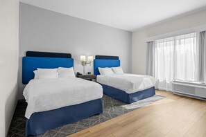 A hotel room with two beds, a nightstand, a lamp, a window with curtains, and a wall-mounted air conditioner. - Hampton Inn & Suites Knightdale Raleigh (Raleigh)