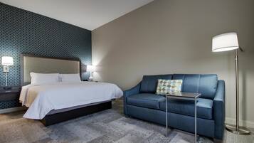 Quarto de hotel com cama, sofá, luminária e parede estampada.