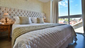 A bedroom with a large bed, a tufted headboard, two bedside tables with lamps, and a view of the outdoors through a large window.