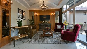 A spacious living room with a fireplace, a large window, and a chandelier. - Hotel Micheline (Gramado)