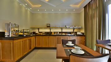 A modern hotel kitchen with wooden cabinets, a buffet counter, and a dining area with a table and chairs.