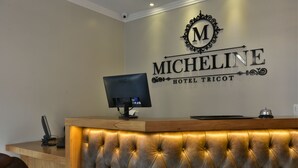 A hotel reception desk with a tufted headboard, a computer monitor, and a sign that reads "MICHELINE HOTEL TRICOT". - Hotel Micheline (Gramado)