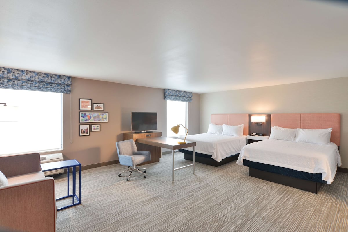 A hotel room with two beds, a desk, a chair, a TV, and framed pictures on the wall.