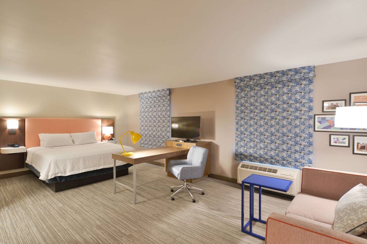 A hotel room with a bed, desk, chair, and a sofa.
