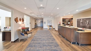 A hotel lobby with a reception desk, seating area, and a blue carpet.